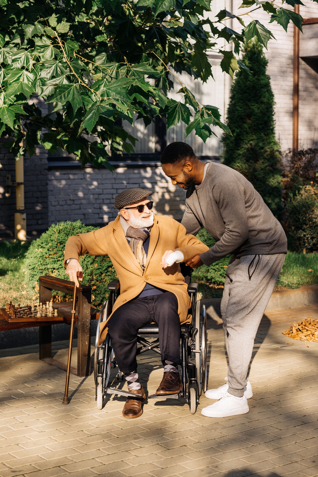 african american man helping senior disabled man to get up from wheelchair on street